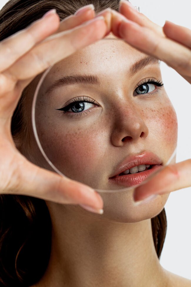 Beauty-Porträt einer Frau mit Glaslinse – Fokus auf natürliche Hautstruktur und klare Augen