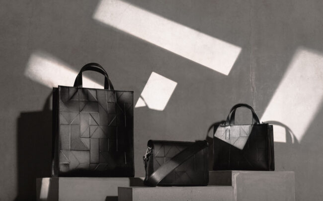 Ecco Kampaign, Drei strukturierte schwarze Designer-Handtaschen in minimalistischem Licht- und Schattenspiel auf Betonhintergrund