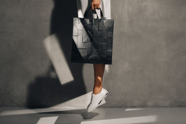 Schwarze Designertasche mit geometrischem Muster, stilvoll präsentiert vor Betonwand mit Schatteneffekten